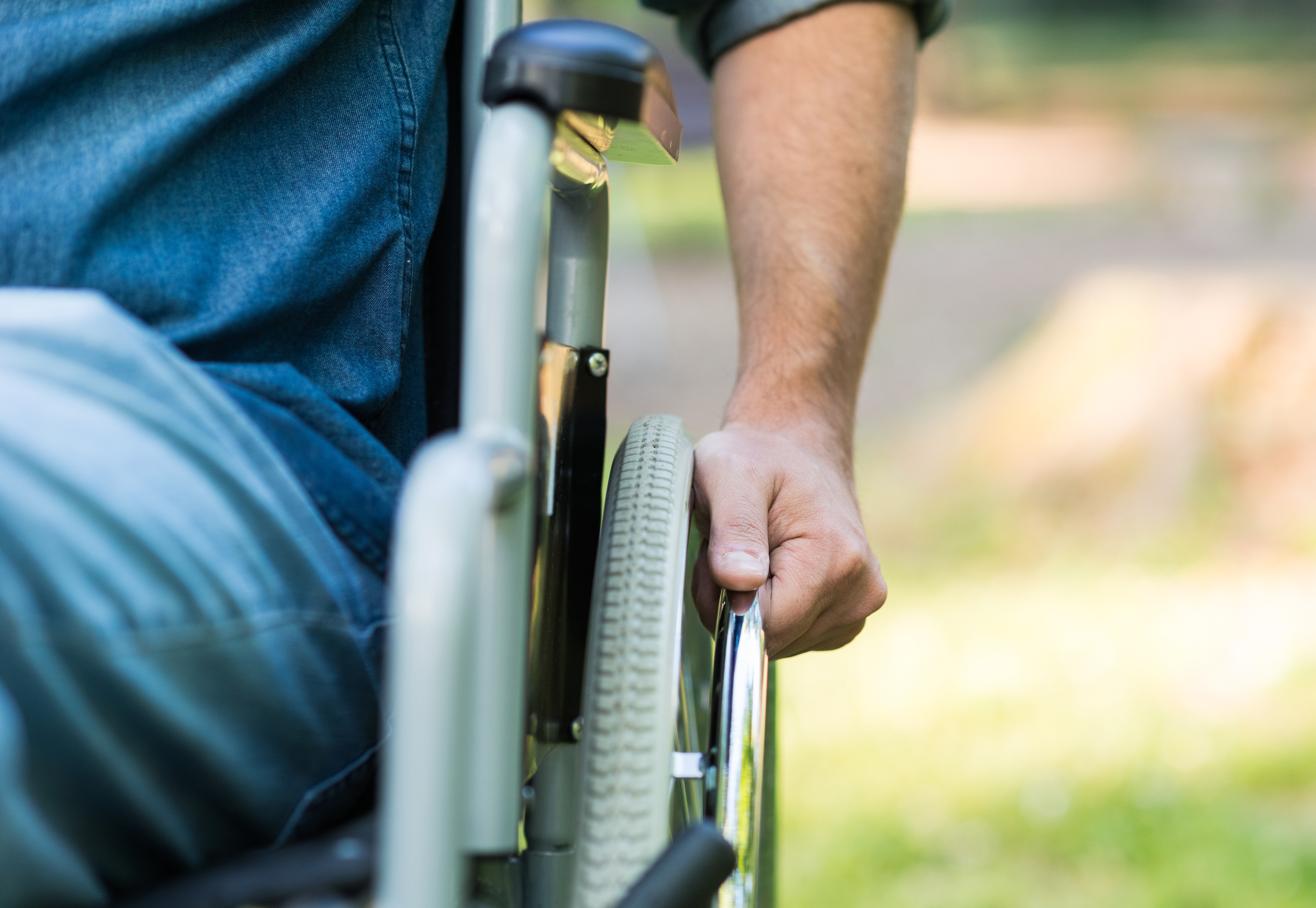 Detail of a man using a wheelchair in a park. Copy-space on the right side
